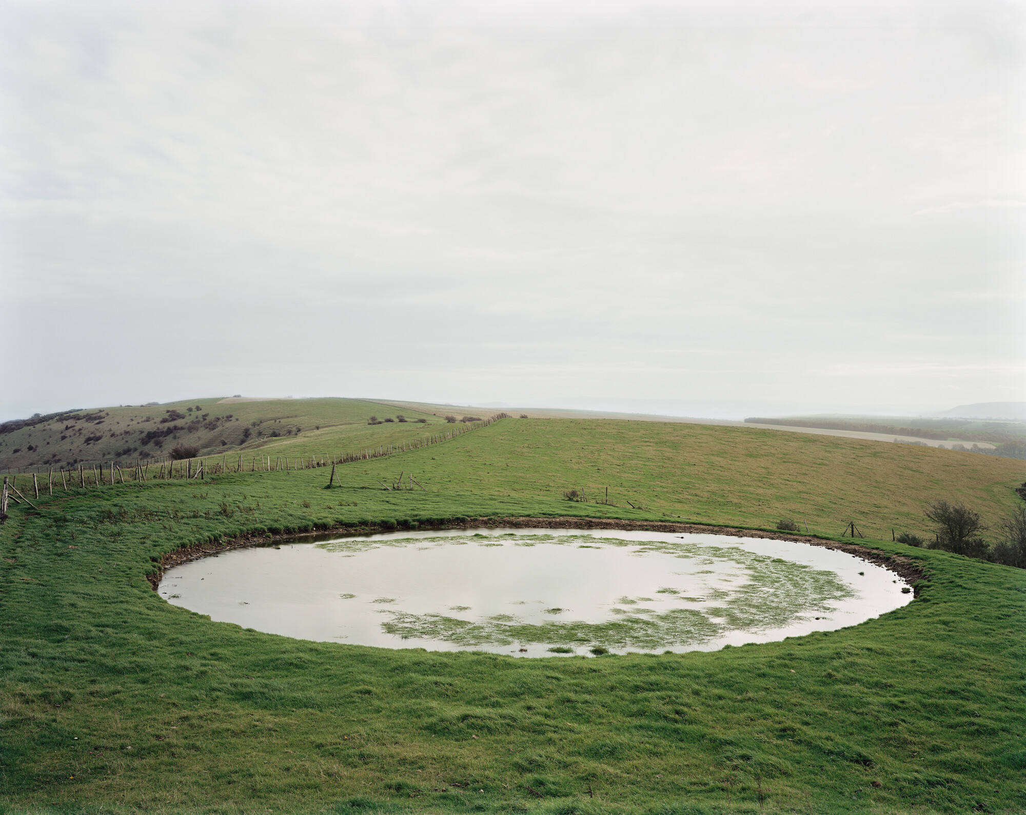 Photograph of a manufactured circular dew pond reflecting a grey sky