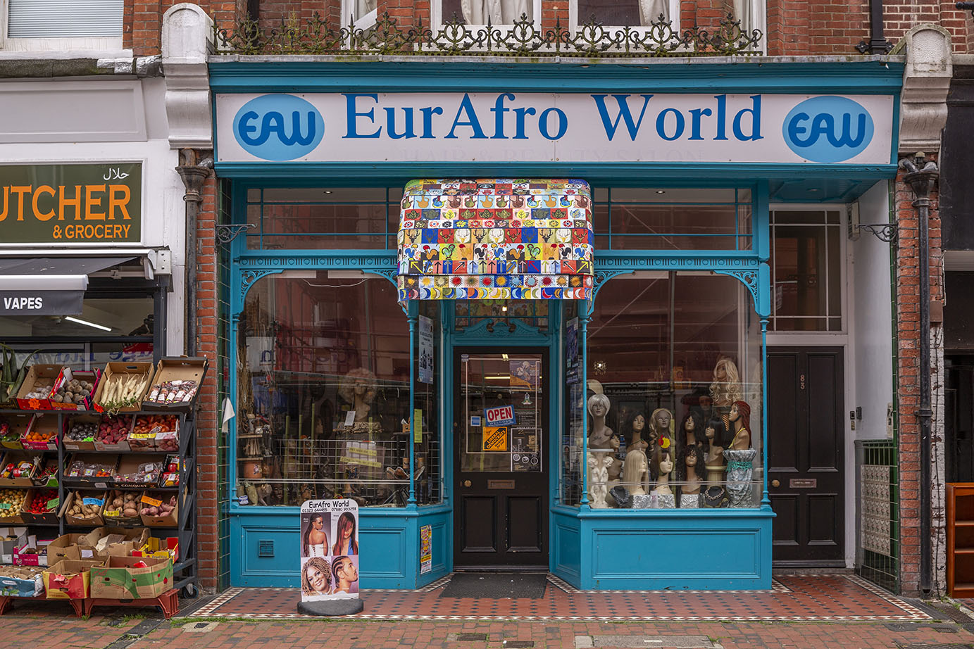 EurAfro World's shop front, which is painted light blue and has an awning made from colourful fabric. The fabric design is made up of tiles with symbols including palm trees, moons, sun and ice cream. 